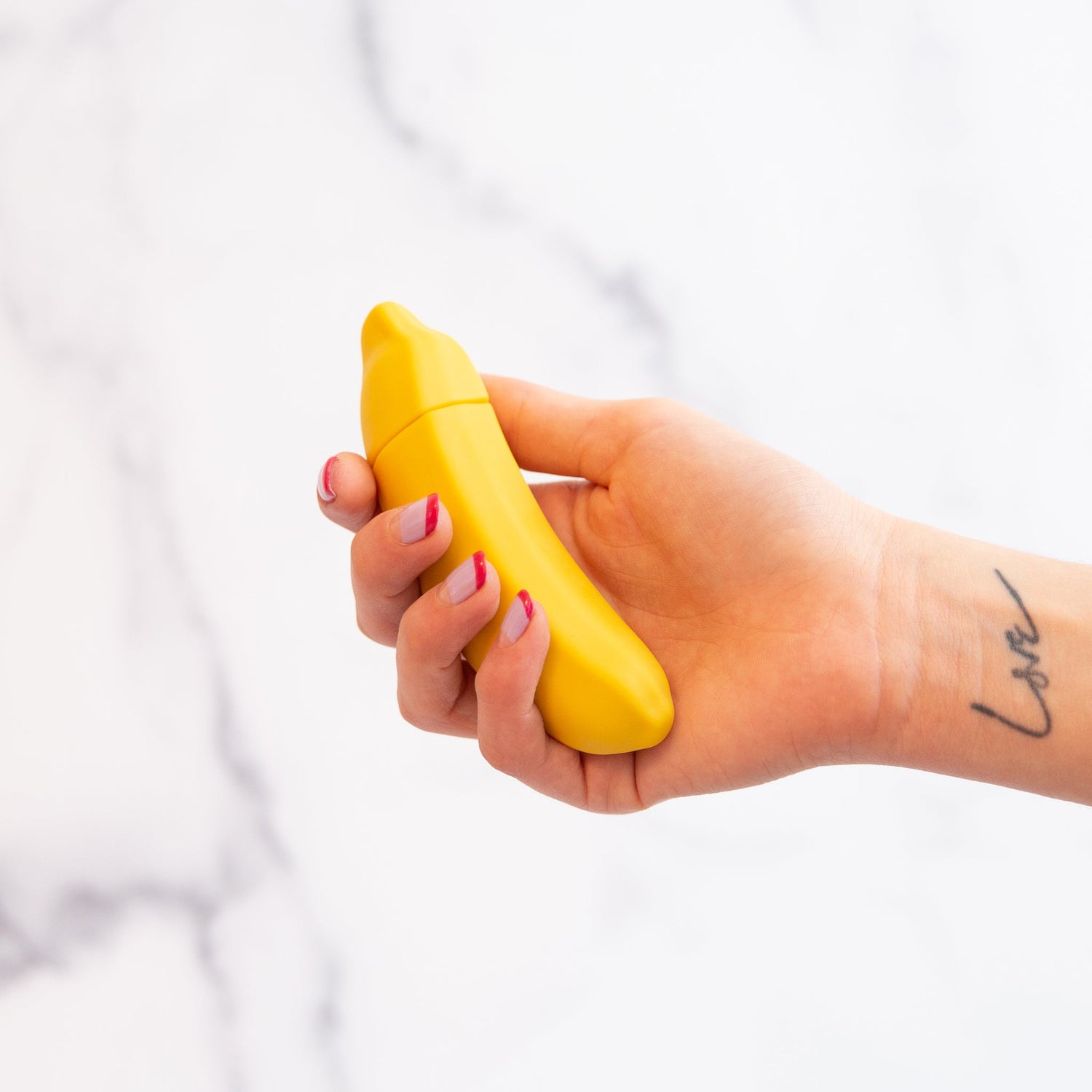 vibrator shaped like a banana held by a hand with love written on it in front of a white background