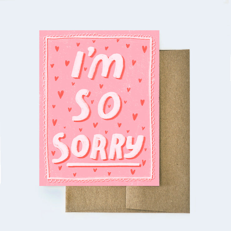 Pink greeting card from Aviate Press that features the text "I'm so sorry" with hand drawn red hearts and a lacey outline. The card is laying on top of a brown kraft paper envelope.