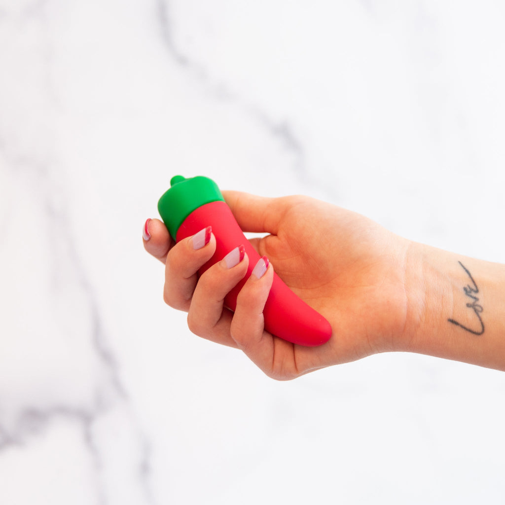 vibrator shaped like a chili pepper emoji held in a hand with a love tattoo on a white background